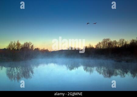 Tôt le matin du printemps au lac, une légère brume plane sur l'eau au début d'une nouvelle journée. Banque D'Images