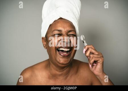 Bonne femme afro senior utilisant le rouleau de jade pendant les soins de la peau spa jour - personnes bien-être concept de style de vie Banque D'Images