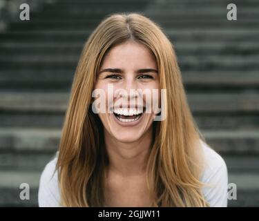 Une jeune femme heureuse souriant dans la caméra tout en étant assise dans les escaliers urbains Banque D'Images