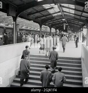 Années 1960, Toyko, Japon, photo historique de cette époque d'une station de métro de Tokyo, avec des navetteurs japonais entrant dans la plate-forme et ceux qui attendent de monter à bord d'un train. La plupart des hommes portent des manteaux de pluie, car le climat subtropical de la ville le voit constamment pleuvoir - bien plus de 100 jours par an. Banque D'Images