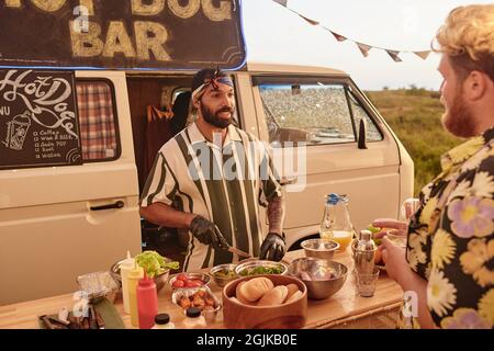 Jeune barbu préparant des sandwichs pour le client lors d'une fête en plein air Banque D'Images