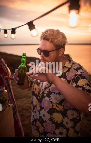 Un jeune homme en lunettes de soleil boit de la bière et danse pendant une fête sur la plage Banque D'Images