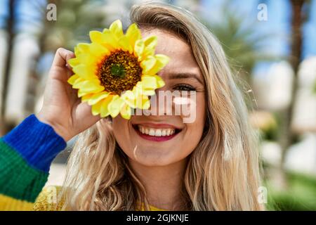 Jeune femme blonde souriant avec du tournesol à l'œil au parc Banque D'Images