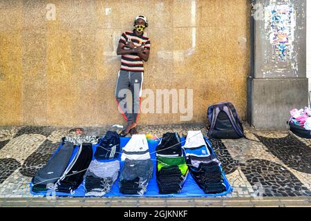 Jeune brésilien vendant des marchandises de marque sur une rue de Niteroi, Rio de Janeiro, Brésil. Il porte un masque de protection. Banque D'Images