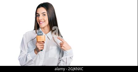 Jeune brune adolescente tenant le microphone du journaliste souriant heureux pointant avec la main et le doigt Banque D'Images