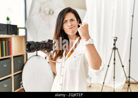 Belle femme caucasienne travaillant en tant que photographe au studio de photographie en colère et folle élevant poing frustré et furieux tout en criant avec colère. r Banque D'Images