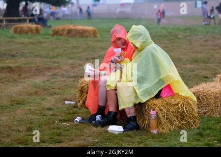 Vicarage Farm, Winchester Hampshire, Royaume-Uni. 10 septembre 2021. Couple dans le poncho de pluie assis parlant, manger et écouter de la musique à Mucky Weekender, Hampshire crédit: Dawn Fletcher-Park/Alamy Live News Banque D'Images