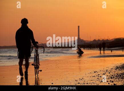 Brighton et la plage de Hove à marée basse. Silhouettes de personnes marchant le long de la plage de sable au coucher du soleil. East Sussex, Angleterre. Shoreham Power Station au loin Banque D'Images