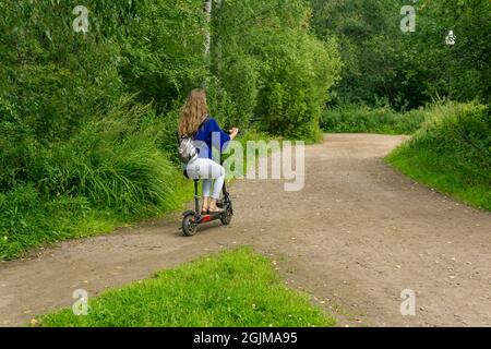 une jeune femme se déplace en scooter électrique le long du chemin à travers le parc Banque D'Images