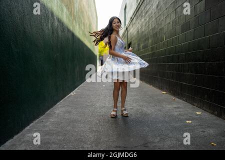 Une adolescente asiatique tourne en robe de fête dans une allée vert foncé Banque D'Images