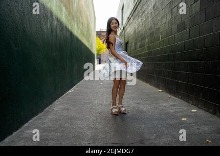 Une adolescente asiatique tourne en robe de fête dans une allée vert foncé Banque D'Images