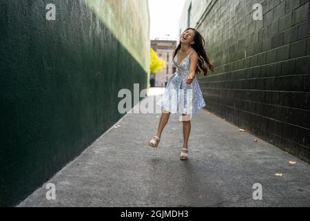 Une adolescente asiatique tourne en robe de fête dans une allée vert foncé Banque D'Images