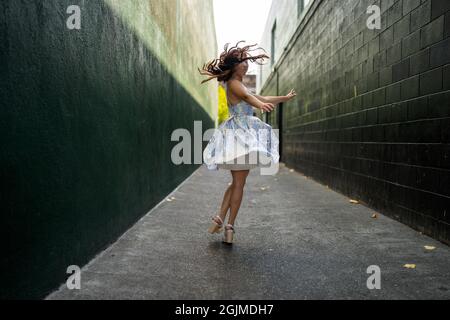 Une adolescente asiatique tourne en robe de fête dans une allée vert foncé Banque D'Images