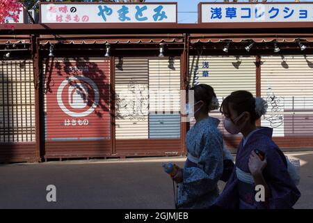 Deux jeunes femmes, portant un kimono et un masque de visage, se promeuxent devant des boutiques touristiques closes dans la zone touristique populaire d'Asakusa Tokyo, au Japon. Banque D'Images