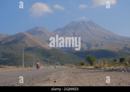 Aksaray.Turquie.Une Audi blanche et un homme sur moto conduite sur route sale avec nuage de poussière derrière elle et magnifique et immense montagne de Hasan Banque D'Images