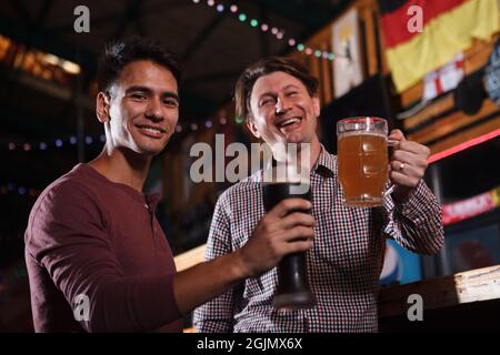 Prise de vue en contre-angle d'amis hommes souriants à l'appareil photo, en grillage avec leurs verres à bière Banque D'Images