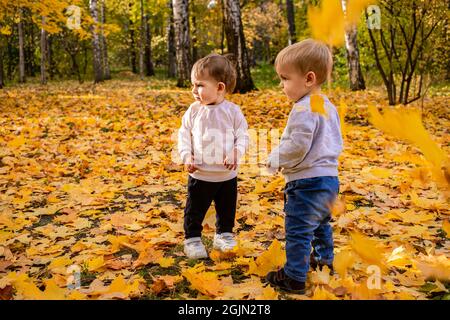 Les enfants gais attrapent des feuilles d'érable tombant dans le parc de la ville d'automne Banque D'Images