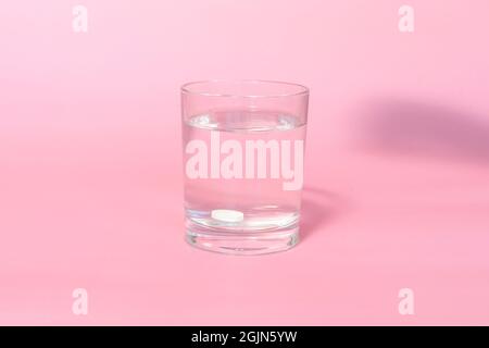 le comprimé se dissout dans un verre d'eau sur fond rose. Banque D'Images