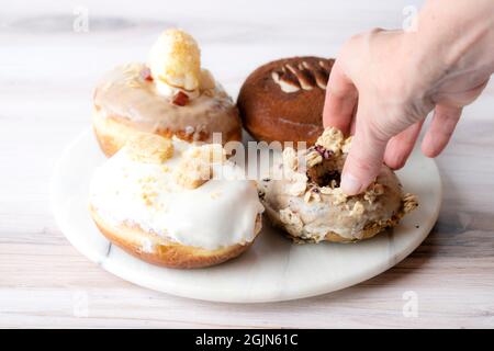 Main saisissant plusieurs types de Donuts sur une plaque de marbre, nourriture Banque D'Images