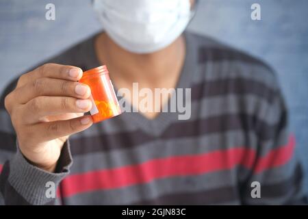 jeune homme dans un masque facial tenant un contenant de pilules médicales Banque D'Images