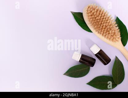 brosse en bois pour le massage corporel anti-cellulite, et bouteille cosmétique sur fond violet clair. Concept de soins du corps Banque D'Images