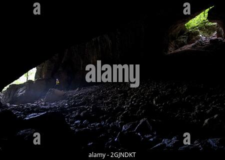 Femme avec un phare debout sur la roche par le ruisseau de rivière sec à l'entrée de la grotte de Tkalca dans le parc de Rakov Skocjan, Slovénie Banque D'Images
