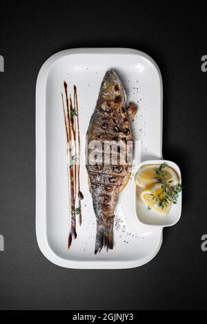 gros plan de poisson farci grillé complet avec du citron sur fond noir Banque D'Images