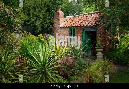 Ancienne maison d'été traditionnelle entourée d'arbustes établis en fleur et d'arbres le matin de l'été à Secret Garden, Beverley, Royaume-Uni. Banque D'Images