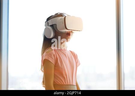 Un enfant s'amuse dans des lunettes blanches de réalité virtuelle, debout sur l'arrière-plan d'une fenêtre. Photo de haute qualité Banque D'Images