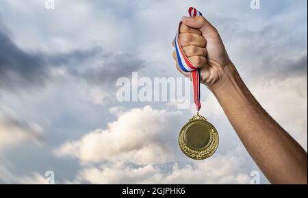 Médaille d'or dans la main du gagnant. Premier prix sur fond ciel nuageux, Sport champion athlète Victory concept. Espace vide et couronne de Laurier, modèle Banque D'Images