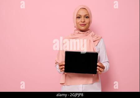 Portrait confiant de arabe musulman belle femme réussie portant le hijab rose debout sur fond rose avec espace de copie et montrant le vide Banque D'Images