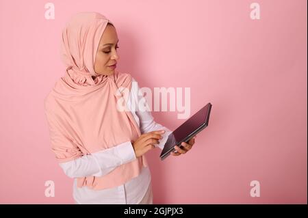 Arabe musulman élégante belle femme avec tête couverte en hijab rose posant sur un fond pastel coloré avec une tablette numérique dans les mains. Por. Isolée Banque D'Images