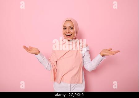 Agréablement surprise magnifique arabe musulmane femme avec tête couverte en hijab rose joyeusement regarder la caméra sourire magnifique et goûtant le sourire torreneux pendant stan Banque D'Images