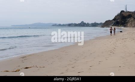 Un couple marche un chien sur la plage de Summerland à Summerland, Californie, États-Unis Banque D'Images