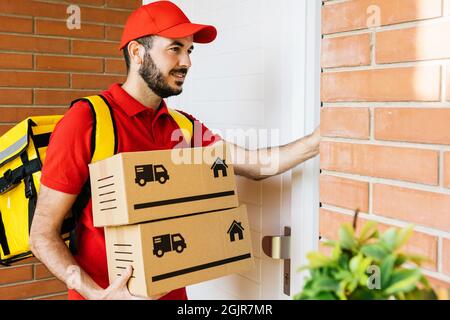 Bon liveur en uniforme rouge avec sac à dos thermique sonnant la sonnette de porte Banque D'Images