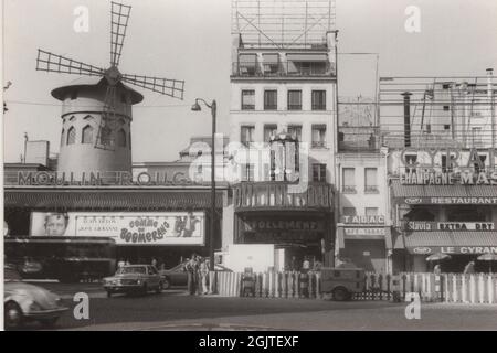 Une photo rétro sur le célèbre et unique théâtre du Moulin Rouge, à Paris Fance des années 1970 ou 1980. C'était un moment très occupé comme il l'a vu sur la photo: Peut-être que c'était un travail de route parce qu'il y a un générateur. Une voiture américaine et une autre VW Beetle sont visibles sur cette photo. Banque D'Images