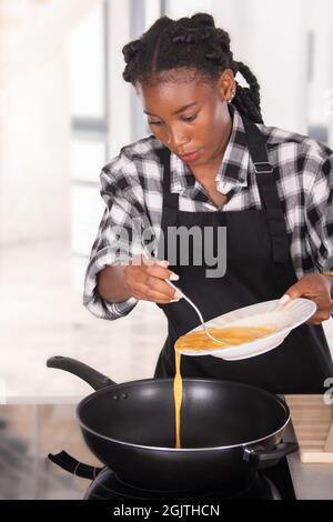 Afro-américaine une femme verse des œufs chuchotés sur une poêle à frire profonde Banque D'Images
