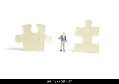 Photographie miniature de personnage de jouet de personnes. Un homme d'affaires haussant debout au milieu de deux pièces de puzzle. Isolé sur fond blanc. Image p Banque D'Images