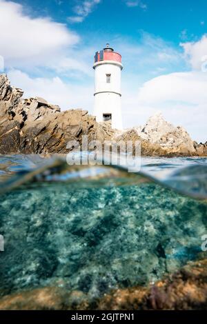 Plan divisé, au-dessus du plan inférieur. Demi ciel, moitié sous l'eau. Vagues défocacées en premier plan avec un phare sur une côte rocheuse. Banque D'Images