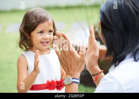 Adorable petite fille en robe bouffie se claquant les mains avec le père quand ils jouent à l'extérieur Banque D'Images