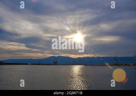 Grues industrielles sur la jetée de la ville de Rijeka, montagne en arrière-plan. Coucher de soleil sur la ville urbaine. Banque D'Images