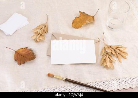 Une carte de visite sur une enveloppe, une lettre ou une invitation sur le fond d'une serviette en lin léger avec des feuilles mortes. Maquette de papeterie de mariage Banque D'Images