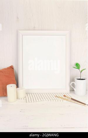 Cadre blanc vide maquette avec petite branche de zamioculcas succulent dans un vase vintage mug sur une ancienne table rustique en bois, avec oreiller, bougies Banque D'Images