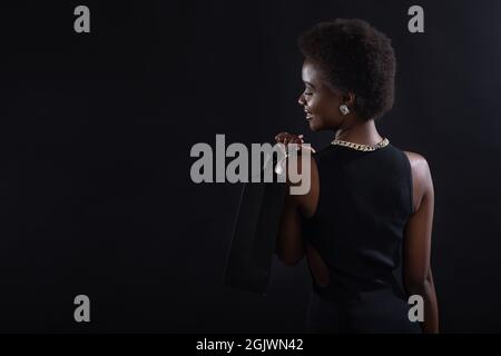 Afro-américaine vue de dos avec la coiffure d'afro tient des sacs de shopping noirs. Vente et réductions sur le marché et le concept du Vendredi fou. Banque D'Images