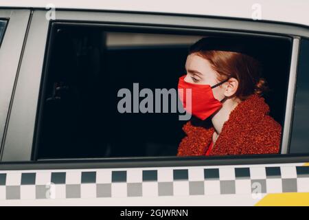 Une jeune femme passager prend un trajet en voiture de taxi pendant la quarantaine pandémique du coronavirus. Femme portant un masque médical stérile. Concept de la distance sociale et de la sécurité sanitaire dans les transports Banque D'Images