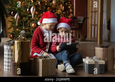 Des petits enfants heureux dans les chapeaux du Père Noël à l'aide d'une tablette numérique. Banque D'Images