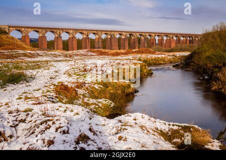 Longue exposition de la grande eau de la flotte entourée de neige en hiver, avec le viaduc ferroviaire en arrière-plan, Dumfries et Galloway, Écosse Banque D'Images