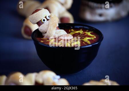 Nourriture amusante pour les enfants. Maman hot dogs sur une table rustique bleue assis à l'intérieur d'un bol de ketchup et de moutarde trempée, avec motif toile d'araignée. Banque D'Images