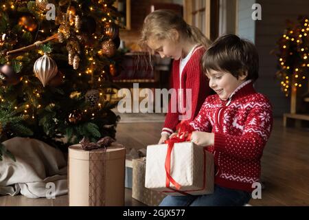 Curieux affectif petits enfants ouvrant cadeaux de Noël. Banque D'Images