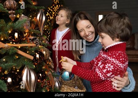 Rire jeune mère appréciant décorer arbre de Noël avec de petits enfants. Banque D'Images